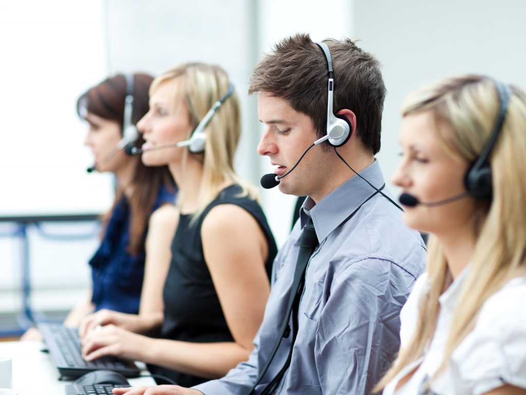 A team of people working at a call center wearing headsets and typing on computers.