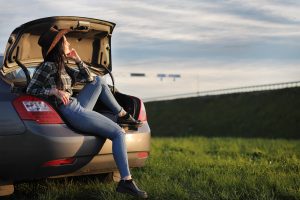 A cowgirl sits on the back of a sedan in the Ohio countryside.