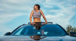 A happy woman breathing fresh air standing on car's sun roof