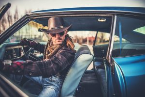 Menacing cowboy sits in the front seat of a muscle car with the door open.